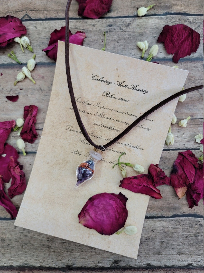 K&ouml;nnte beinhalten: Eine kleine Glasflasche gef&uuml;llt mit Amethystkristallen, Rosenquarz und anderen Kristallen h&auml;ngt an einem braunen Lederband. Die Flasche ist mit "Calming, Anti-Anxiety, Relieve stress!" beschriftet und listet die Vorteile von Amethyst und Lavendel auf.