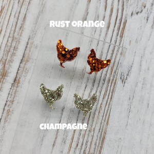 May include: Two pairs of glitter chicken earrings. One pair is rust orange and the other pair is champagne.