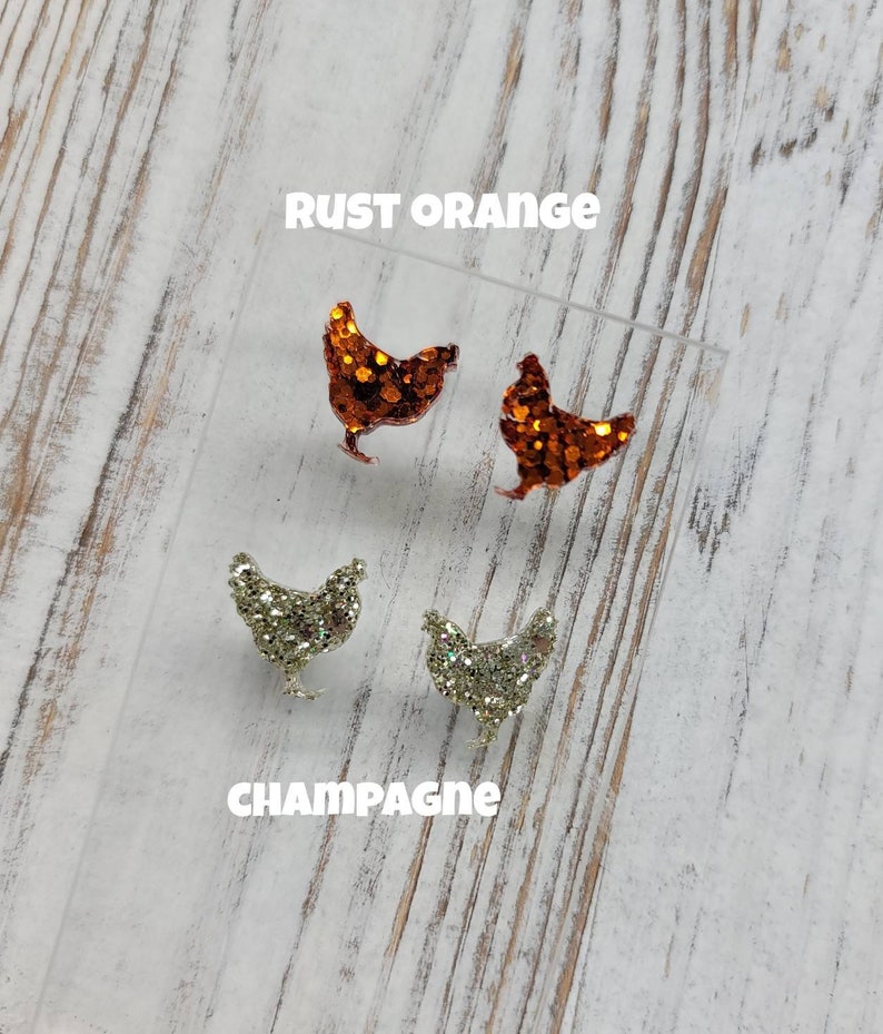 May include: Two pairs of glitter chicken earrings. One pair is rust orange and the other pair is champagne.