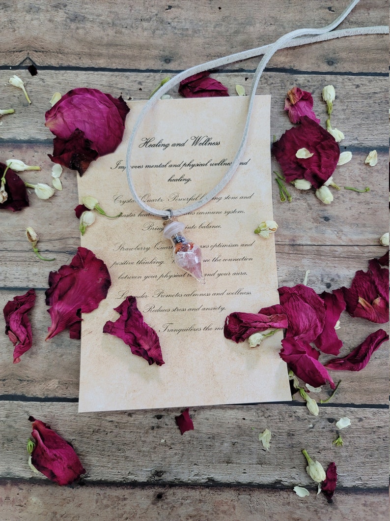May include: A white leather cord necklace with a pink and red crystal pendant. The pendant is surrounded by dried rose petals and white flowers. The text on the card reads "Healing and Wellness" and describes the benefits of the crystal.