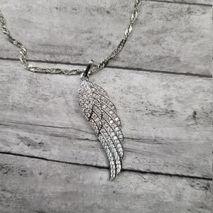 Pode incluir: Um colar de corrente de prata com um pingente de asa de prata incrustado com pedras de zirc&ocirc;nia c&uacute;bica transparentes.