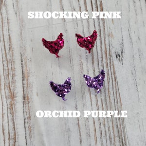 May include: Two pairs of glitter chicken earrings. The first pair is shocking pink and the second pair is orchid purple.