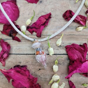 May include: A white leather cord necklace with a clear glass bottle pendant filled with pink, orange, and blue crystals and dried flowers.
