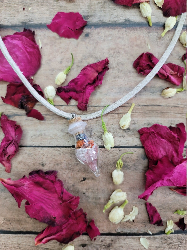 May include: A white leather cord necklace with a clear glass bottle pendant filled with pink, orange, and blue crystals and dried flowers.