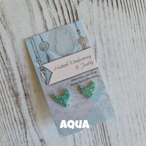 May include: A pair of aqua blue glitter bird earrings on a card with the text "Hastrich Woodworking & Jewelry" and "www.etsy.com/shop/hastrichwoodworking" and the word "AQUA" in large letters.
