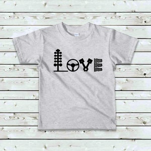 May include: A grey t-shirt with a black graphic design that says "LOVE" using car parts as letters. The letters are a tree, a steering wheel, a piston, and a chequered flag.