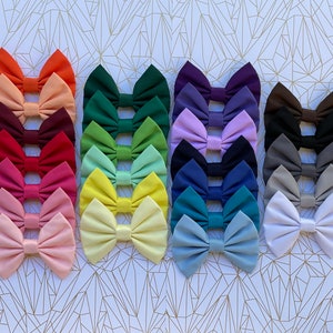 Può includere: Un set di 20 fiocchi per capelli in tessuto di vari colori, tra cui rosso, verde, blu, giallo e rosa. I fiocchi sono disposti in file, con ogni fila che presenta un colore diverso.