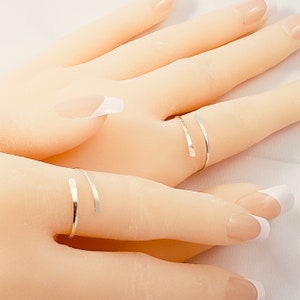 May include: Two silver rings on a hand with white nail polish. The rings are thin and delicate, and they are wrapped around the fingers.