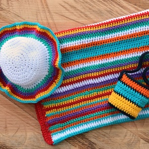 May include: A set of crocheted items in rainbow colors, including a hat, a blanket, and a small bag. The items are made with a variety of colorful yarns and have a striped pattern.