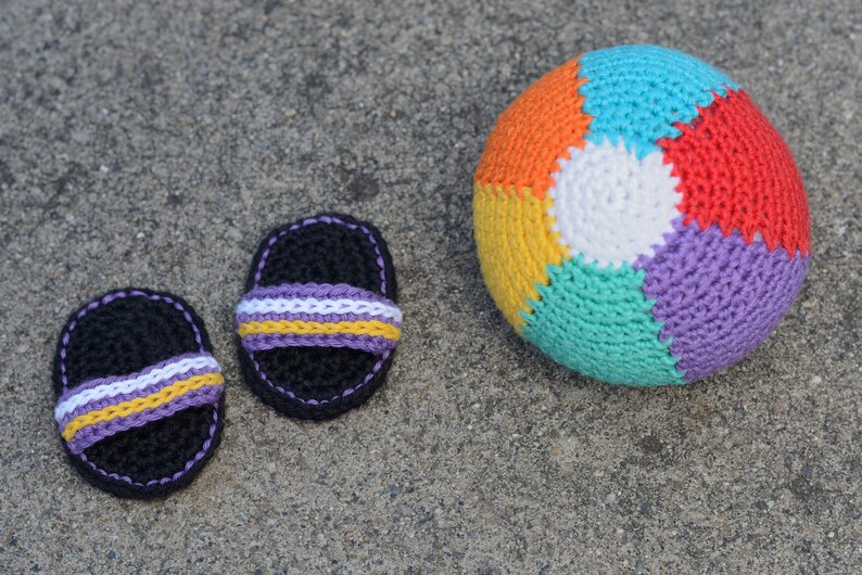 May include: Two crocheted black sandals with purple, white, and yellow stripes and a multi-colored crocheted beach ball.