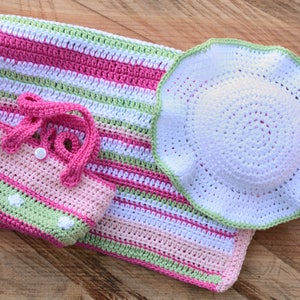 May include: A set of crocheted baby items in pink, green, and white. The set includes a blanket, a hat, and a small bag.
