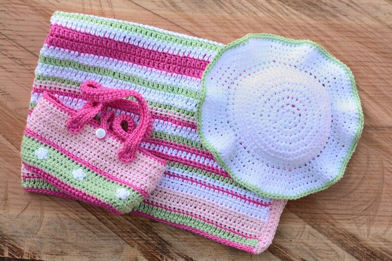 May include: A set of crocheted baby items in pink, green, and white. The set includes a blanket, a hat, and a small bag.
