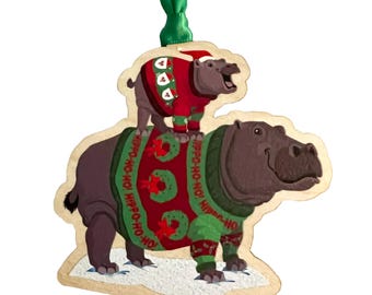 May include: Wooden Christmas ornament featuring two hippos. The larger hippo wears a green and red sweater with the text "HIPPO-HO-HO!" and a wreath design. A smaller hippo sits on top, also wearing a red sweater and Santa hat.