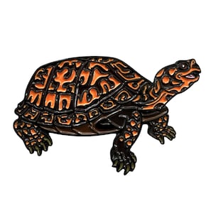 May include: A detailed, stylized turtle figurine. The turtle's shell features a dark brown base with an intricate orange pattern. The head and legs are dark brown, and the turtle is set against a white background.