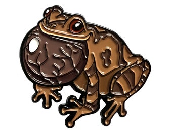 May include: A brown and black enamel pin of a cartoon frog with a large, round eye. The frog is sitting on its hind legs with its front legs outstretched.