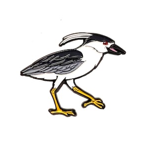 Op de afbeelding: Een geëmailleerde pin van een vogel met een wit lichaam, zwart-grijze vleugels en gele poten. De vogel heeft een zwarte snavel en een rood oog, tegen een witte achtergrond.
