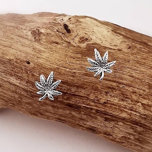 Puede incluir: Un par de pendientes de plata con forma de hoja de marihuana. Los pendientes son pequeños y delicados, y son perfectos para añadir un toque de fantasía a cualquier atuendo.