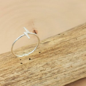 Op de afbeelding: Een zilveren ring met een bliksemontwerp. De ring ligt op een houten oppervlak.