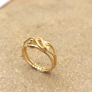 Puede incluir: Un anillo de tono dorado con acabado pulido y un diseño intrincado de varias capas. La banda consta de varios hilos finos e interconectados que se superponen y se entrelazan para formar un punto focal elevado y escultural.
