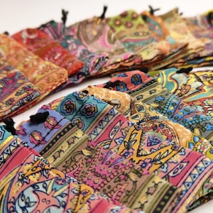 Può includere: Una collezione di sacchetti colorati con coulisse e intricati motivi paisley. Le borse presentano una varietà di colori, tra cui rosa, arancione, blu e verde, con coulisse nere. Il tessuto sembra morbido e leggero.