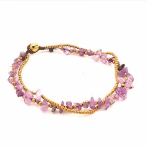 May include: A delicate anklet with a double strand of small gold beads and purple gemstone chips. The anklet has a small gold bell charm.
