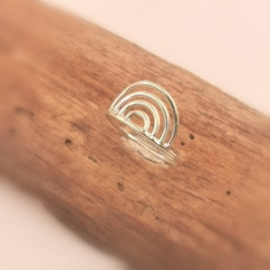 Puede incluir: Un anillo de plata con un diseño de arcoíris. El anillo está hecho de múltiples bandas delgadas de plata que se apilan una encima de la otra para formar una forma de arcoíris.