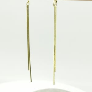 Pode incluir: Um par de brincos de ouro pendurados com três barras finas verticais penduradas em cada brinco.