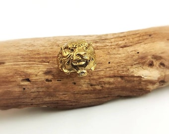 May include: A gold-colored ring with a detailed tiger head design. The ring is sitting on a piece of driftwood.