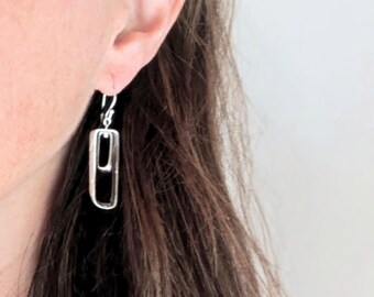 May include: Silver dangle earrings with a geometric design. The earrings feature two interlocking rectangular shapes.