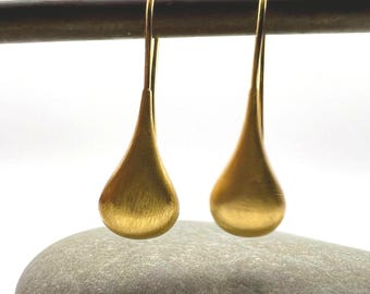 Puede incluir: Un par de pendientes dorados en forma de lágrima. Los pendientes cuelgan de una barra marrón oscuro, con una piedra gris en primer plano. Los pendientes tienen un acabado de metal cepillado y un diseño sencillo y elegante.