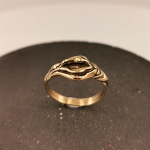 May include: A gold-toned ring with a unique, abstract design. The ring is made of metal and has a smooth, polished finish.