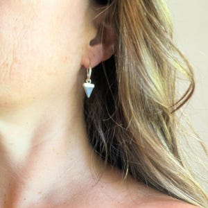 Puede incluir: Pendientes de aro de plata con forma de triángulo. Los pendientes son pequeños y delicados.