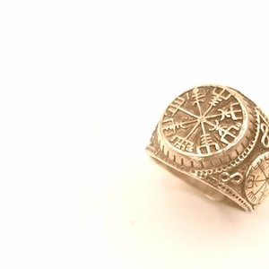 Puede incluir: Un anillo de plata con un diseño detallado que presenta una rosa de los vientos y otros símbolos. El anillo es una banda ancha con un diseño en relieve.