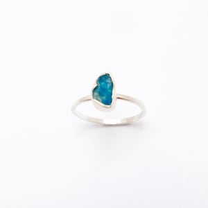 May include: A silver ring with a blue gemstone set in the centre. The gemstone is a rough, irregular shape.