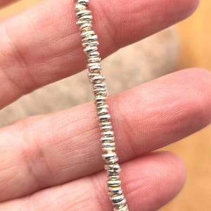 May include: A single strand of small, metallic silver-colored beads arranged in a vertical line. Each bead features a slightly irregular, flattened circular shape with a reflective surface, creating a uniform texture along the entire length of the strand.