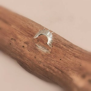 Könnte beinhalten: Ein silberner Ring mit einem Sonnenstrahl-Design. Der Ring ist aus Metall und hat eine glatte Oberfläche.