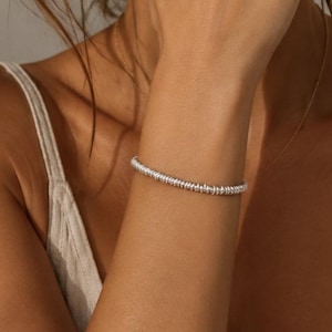 May include: A silver bracelet composed of numerous small, uniform, disc-shaped beads strung together in a continuous circular band. The metallic beads feature a reflective surface and are arranged tightly to create a textured, beaded appearance.