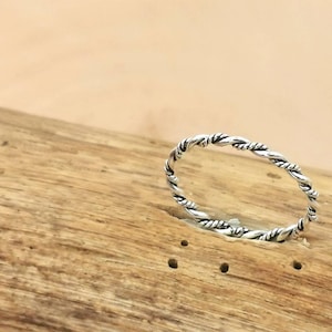 Puede incluir: Un anillo de banda torcido de plata sobre una superficie de madera.