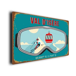 Könnte beinhalten: Ein Vintage-Schild aus Metall mit blauem Hintergrund und einem Skifahrer mit Skibrille. Das Schild trägt die Aufschrift "Val d'Isere" und die Koordinaten 46.5667° N, 11.7167° E.