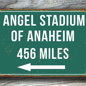 May include: A green metal sign with white text that reads "Angel Stadium of Anaheim 456 Miles" with a white arrow pointing to the left.