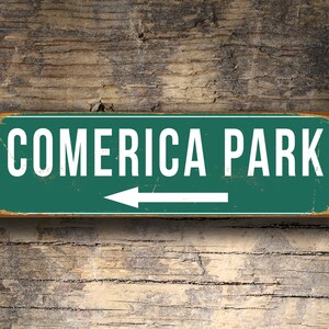 May include: A green and white metal sign with the text "Comerica Park" and a white arrow pointing to the left.