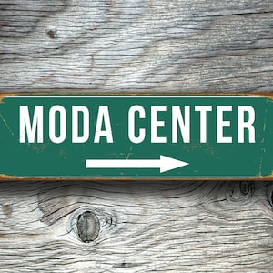 Könnte beinhalten: Ein grünes Metallschild mit weißem Text, auf dem "MODA CENTER" steht, und einem weißen Pfeil, der nach rechts zeigt.