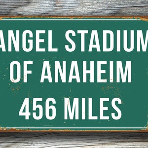 May include: A vintage-style metal sign with a green background and white text. The sign reads "Angel Stadium of Anaheim 456 Miles".