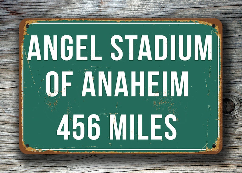 May include: A vintage-style metal sign with a green background and white text. The sign reads "Angel Stadium of Anaheim 456 Miles".