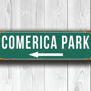 May include: A green metal sign with white text and an arrow pointing left. The sign reads "Comerica Park".