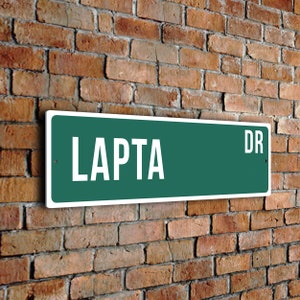 May include: A green street sign with white lettering that reads "LAPTA DR". The sign is mounted on a brick wall.