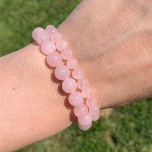 May include: A pink rose quartz beaded bracelet with a stretchy band. The bracelet is made of round beads and is worn on a person's wrist.