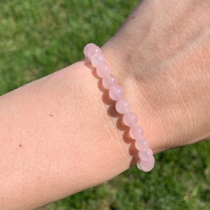 May include: A pink rose quartz beaded bracelet. The bracelet is made of small, round beads that are strung together on a clear elastic cord.