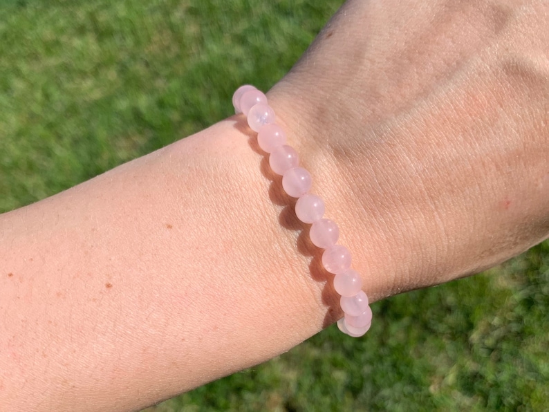 May include: A pink rose quartz beaded bracelet. The bracelet is made of small, round beads that are strung together on a clear elastic cord.
