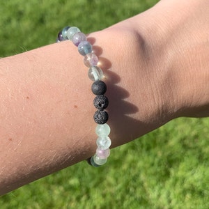 May include: A bracelet made with green, purple, and clear fluorite beads and black lava rock beads.
